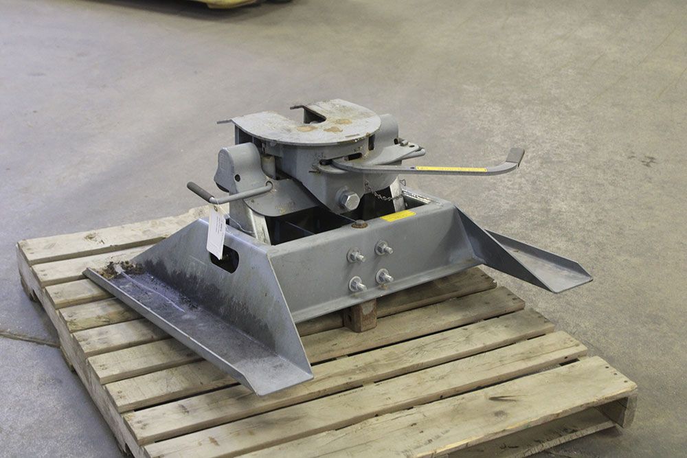 A fifth wheel trailer hitch, gray metal, mounted on a wooden pallet, with a handle and safety features.