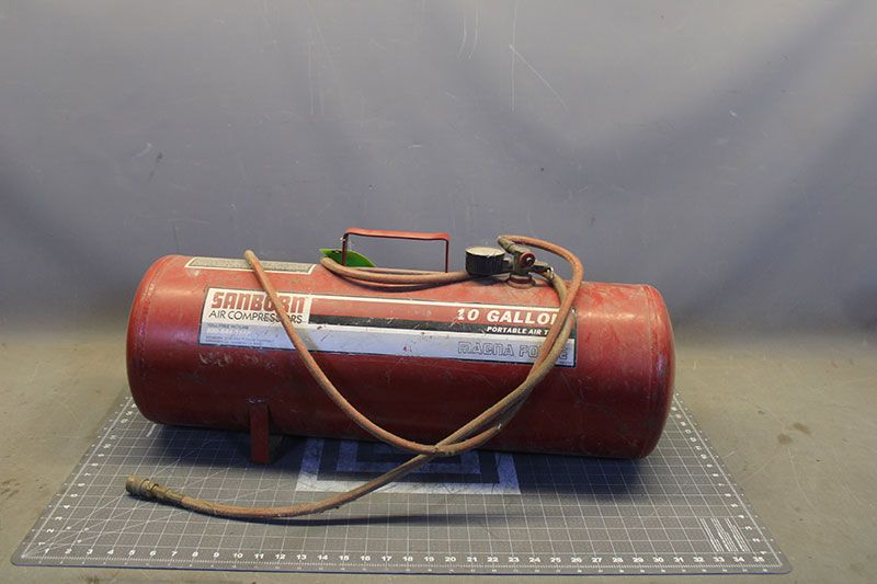 Red 10-gallon air compressor with hose and handle, sitting on a gridded surface.