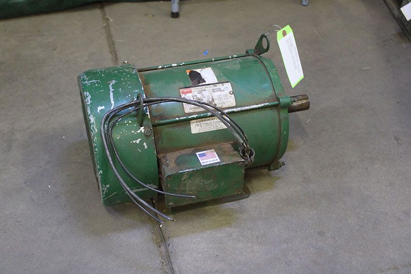 Green electric motor on concrete floor with attached wires and label.