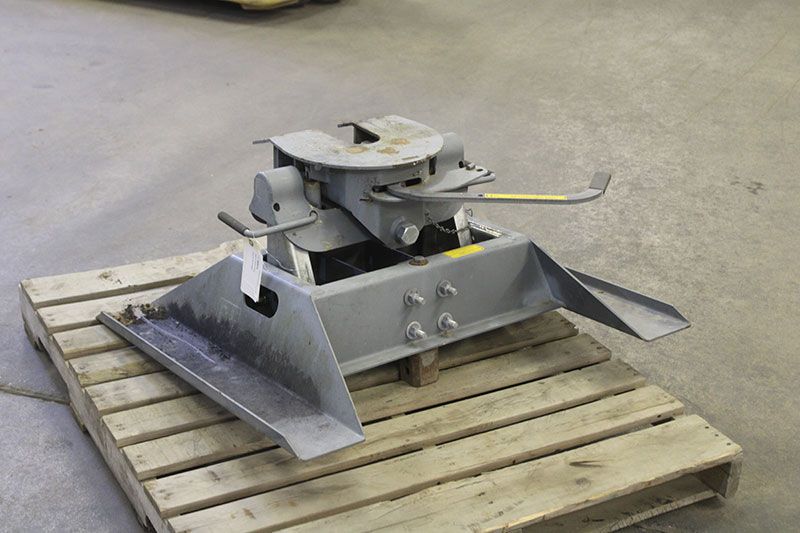 A gray fifth-wheel coupling on a wooden pallet, designed for attaching a trailer to a semi-truck.
