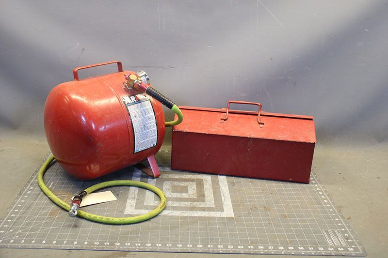 Red air tank with hose and toolbox on a patterned mat.