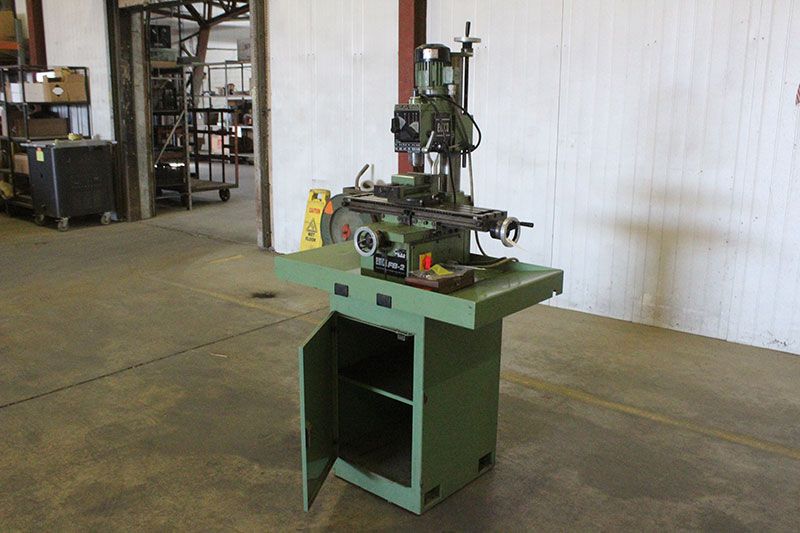 Green industrial machine tool on a stand with a open storage cabinet in a workshop.