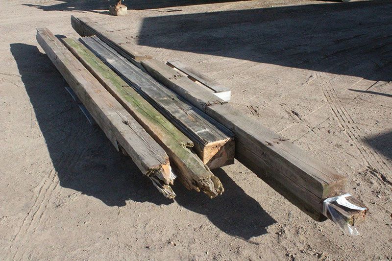 Pile of weathered wooden beams on a dirt surface, varying in size and color.