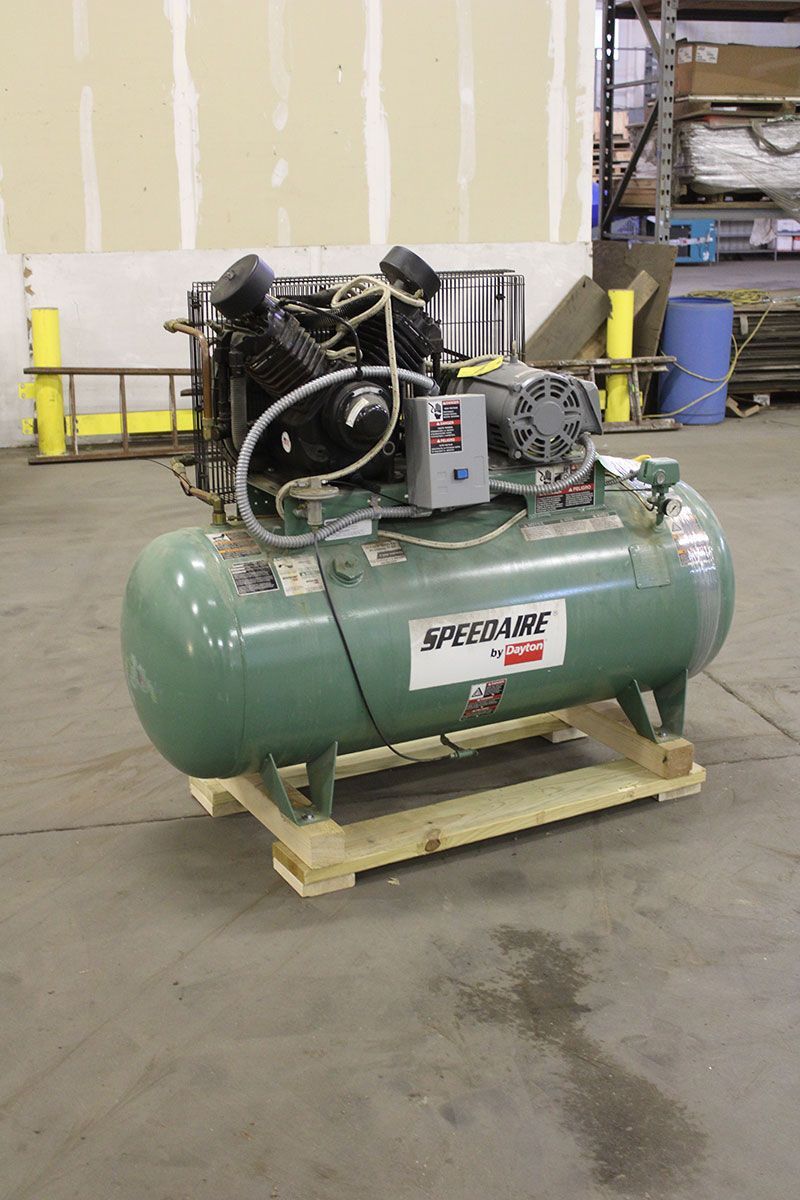 Green industrial air compressor on a wooden pallet in a warehouse.