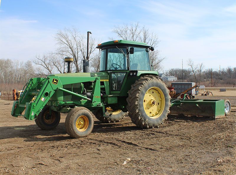 Green John Deere tractor with loader and a box blade on a farm.