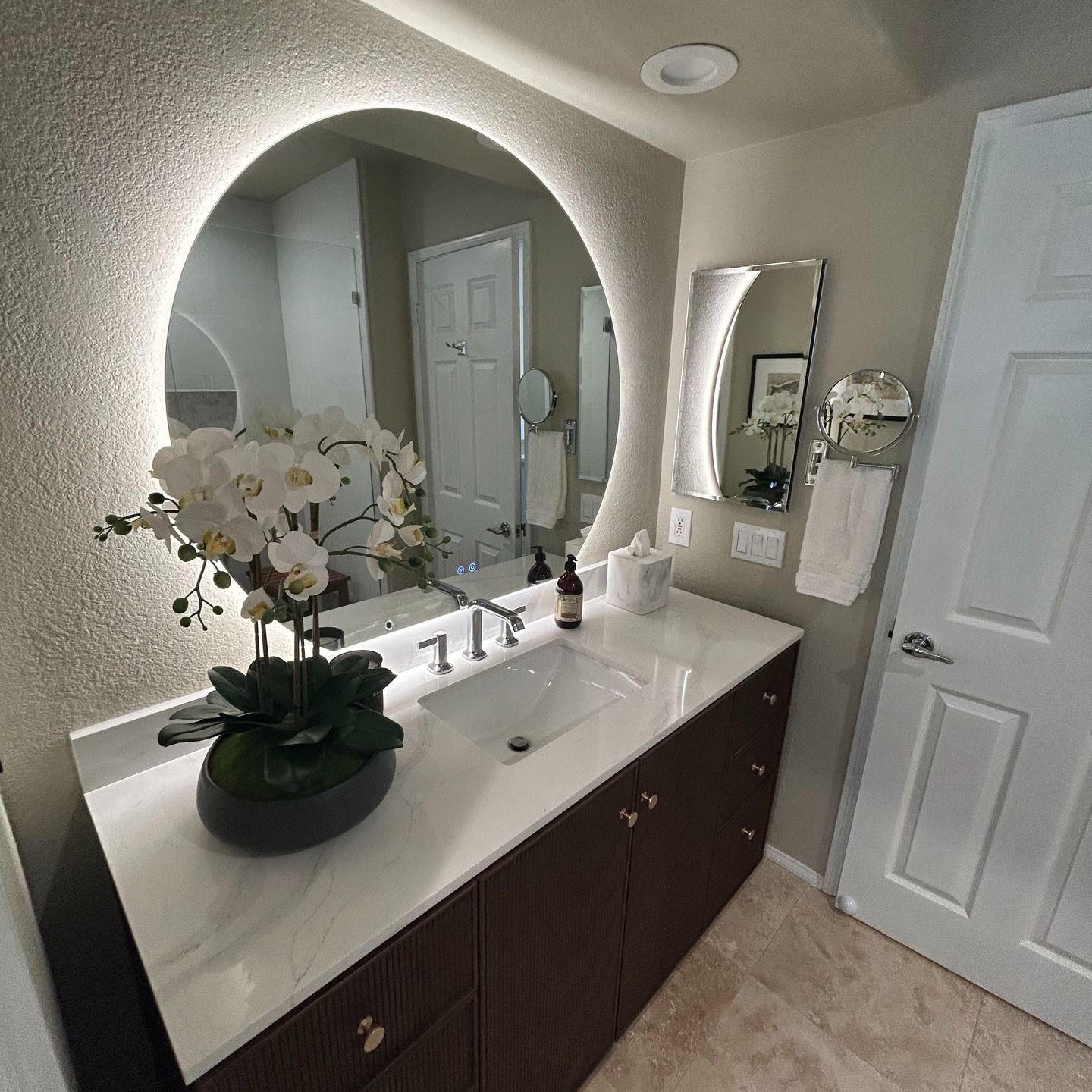 Modern bathroom vanity with round mirror, white countertop, orchid, and dark wood cabinets