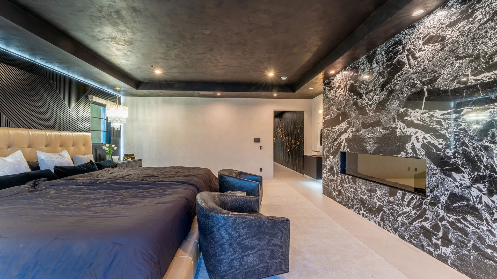 Modern bedroom with dark ceiling, large bed, blue chairs, and abstract black-and-white wall art