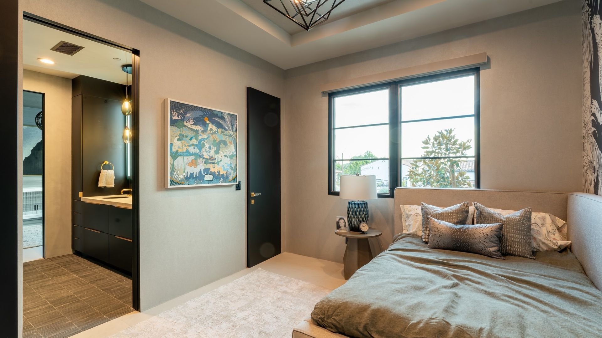 Modern bedroom with a bed, window, artwork, and an open doorway to a bathroom