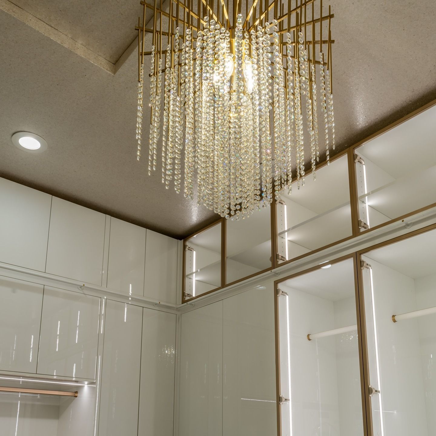Modern bathroom with glossy white cabinets and a gold crystal chandelier ceiling light