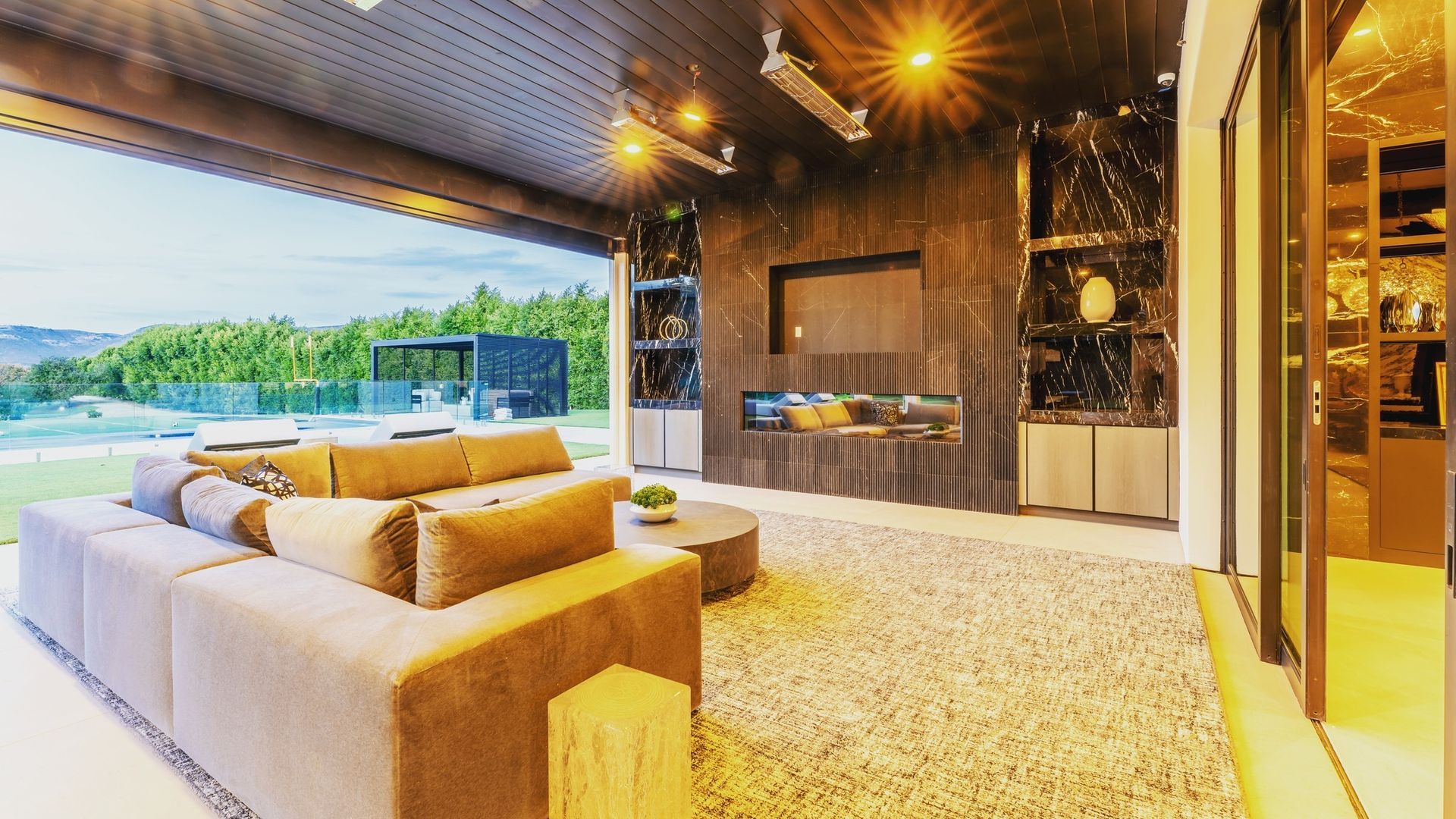 Modern covered patio with sectional sofa, fire pit, and open view of a grassy landscape.
