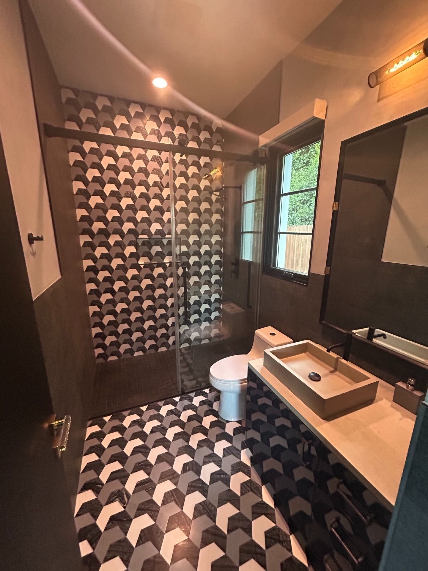 Modern bathroom with black-and-white patterned tile, shower, vanity sink, and window light