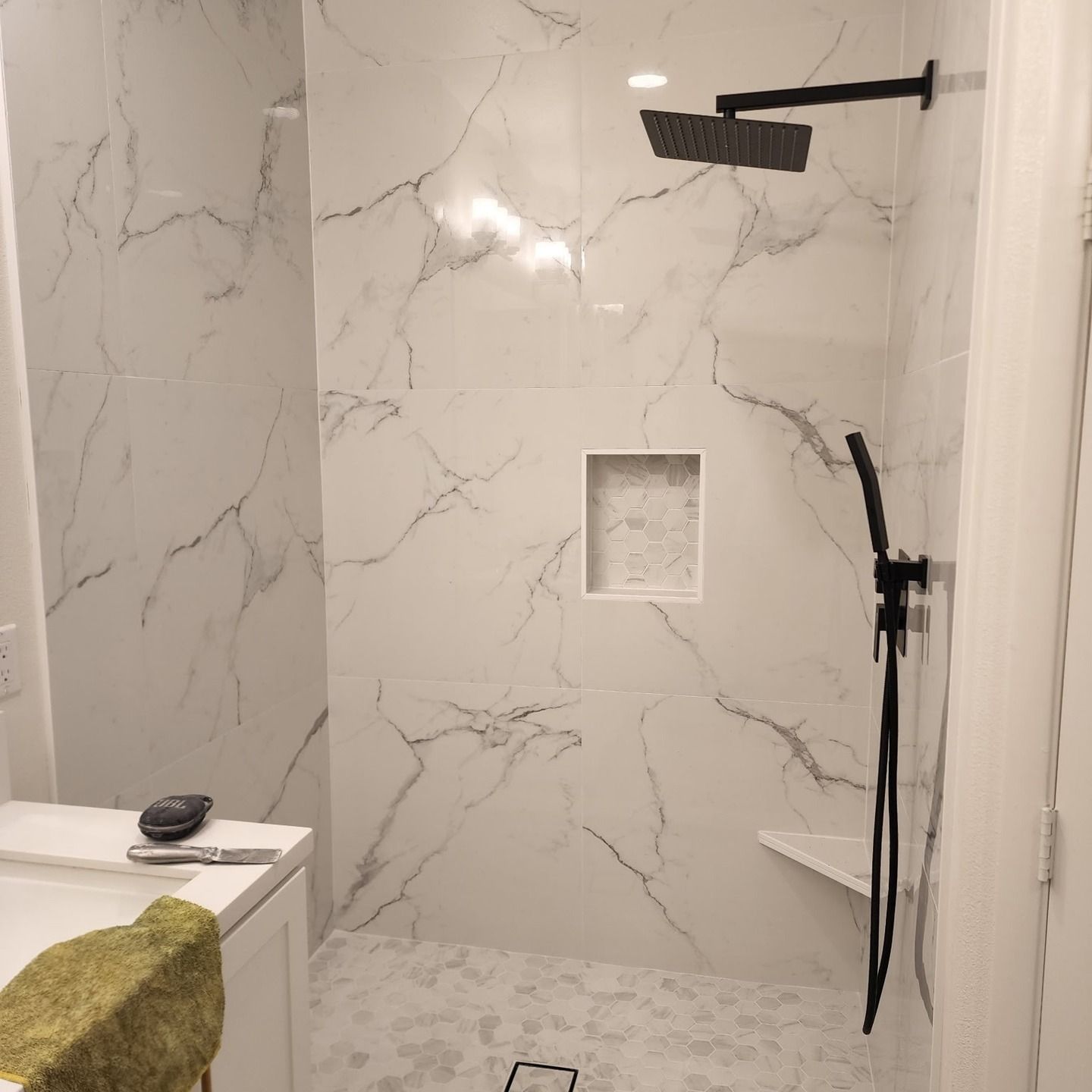Modern marble-tiled shower with black fixtures and a recessed shelf in a bathroom