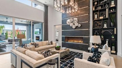 Modern luxury living room with a fireplace, beige sofas, black patterned rug, and wall decor