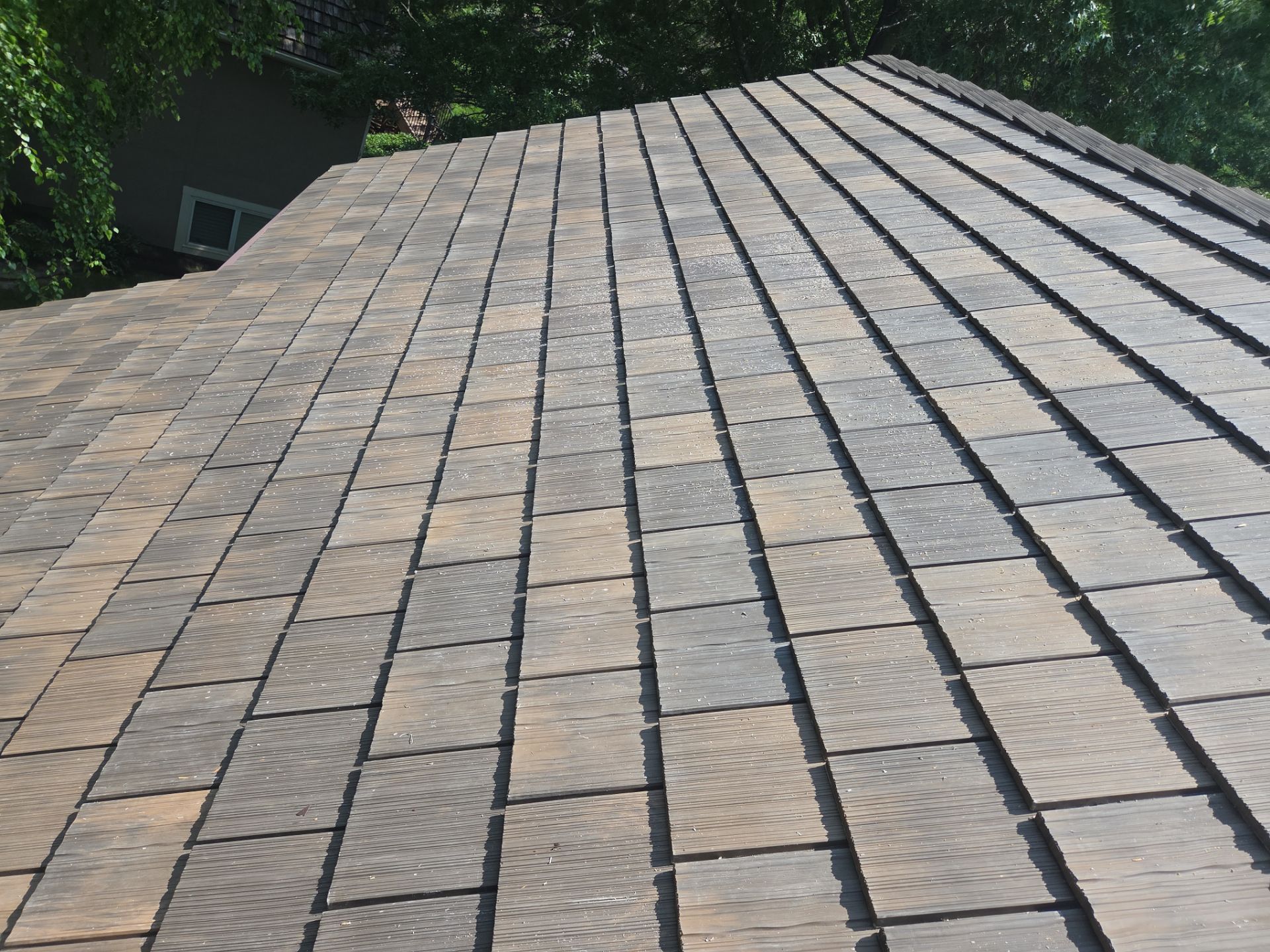 Brown and gray shingled rooftop of a house with trees visible in the background.