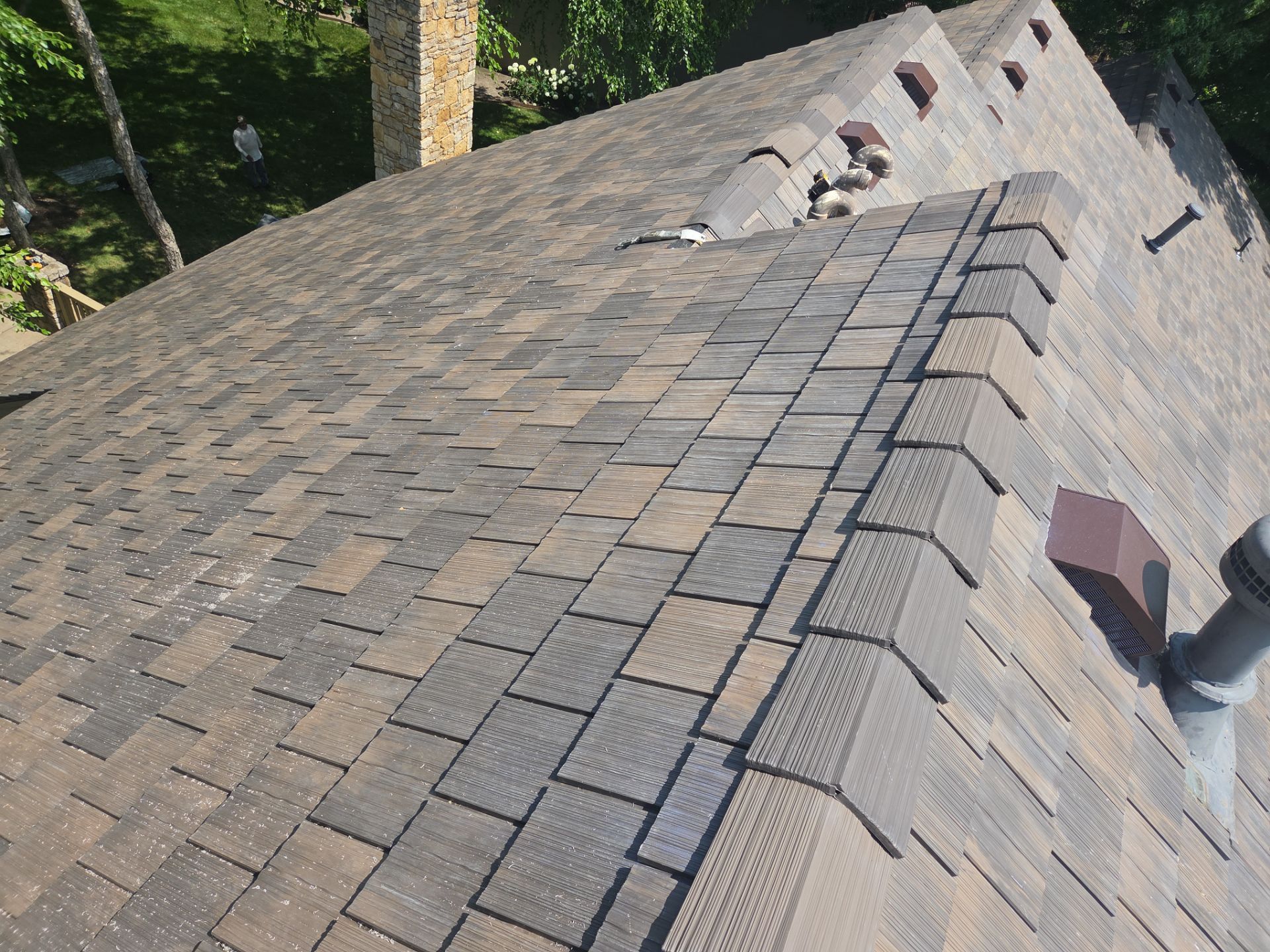 Close-up of a brown shingled roof with some dark-colored shingles, and a chimney.
