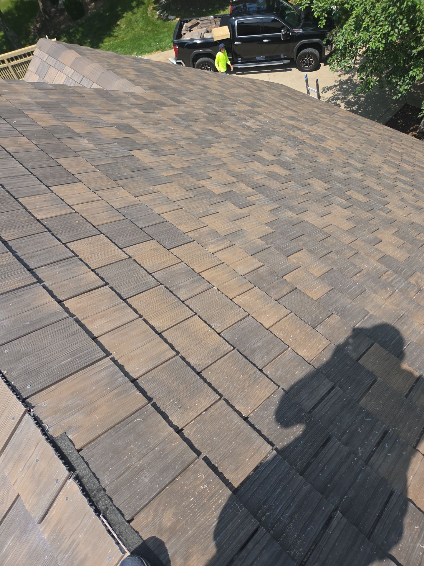 Roof with gray and tan shingles, a black truck, and a person in a yellow vest.