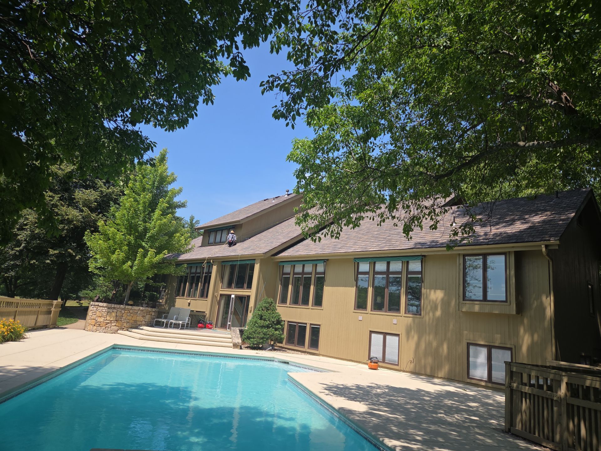 A large house with a pool surrounded by trees on a sunny day.