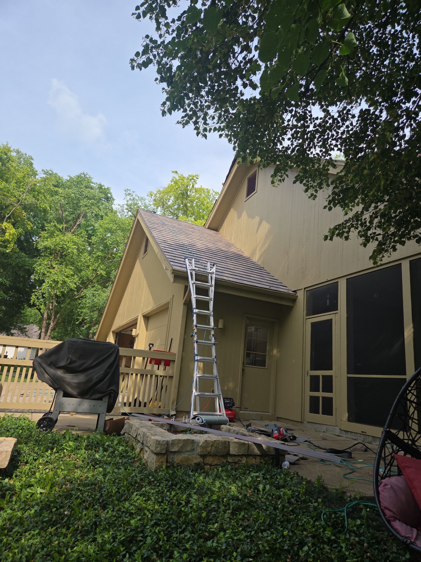 A ladder leans against a house with a metal roof. Deck, yard, and trees.
