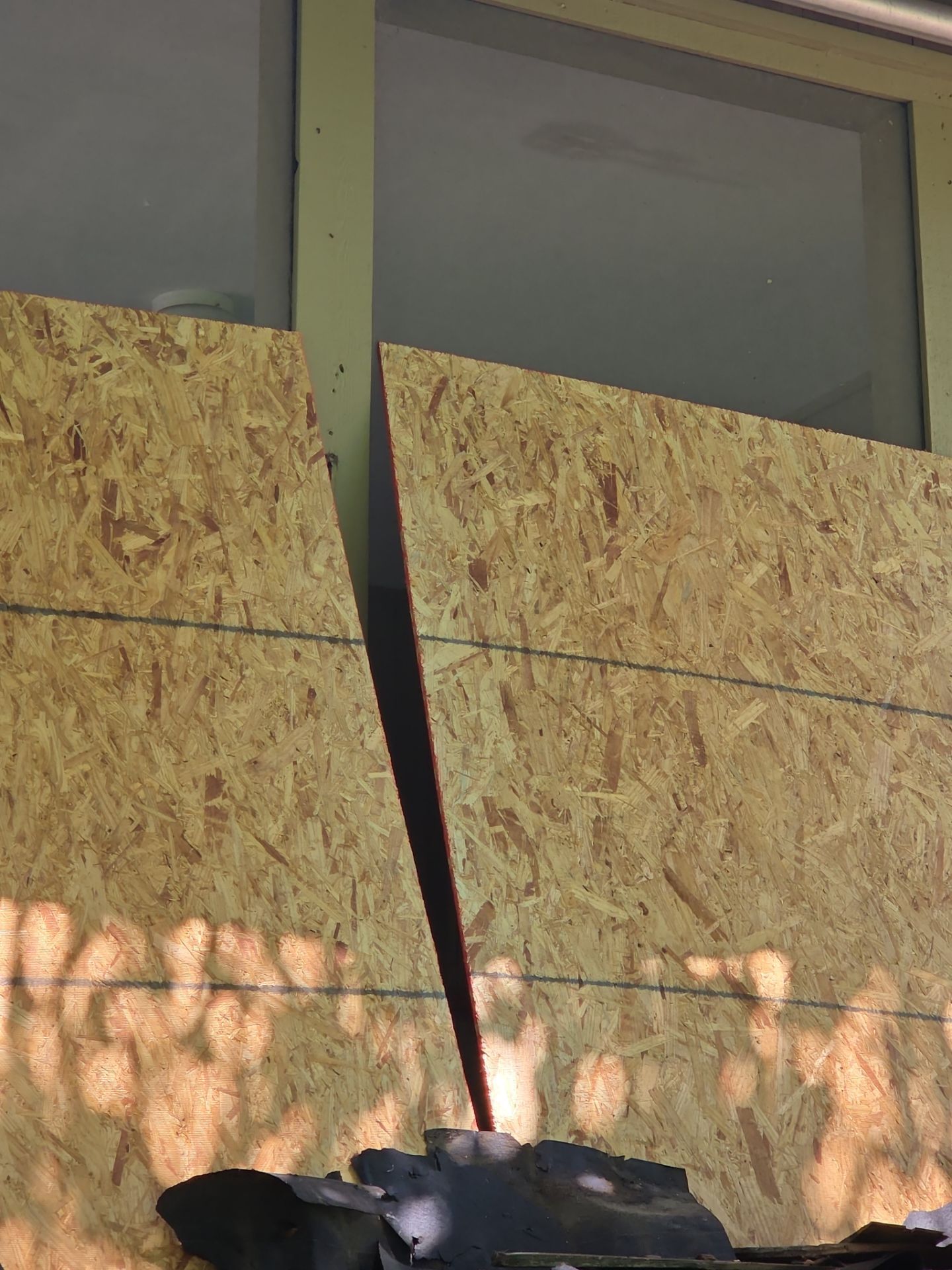 OSB boards covering a window, sunlight casting shadows below.