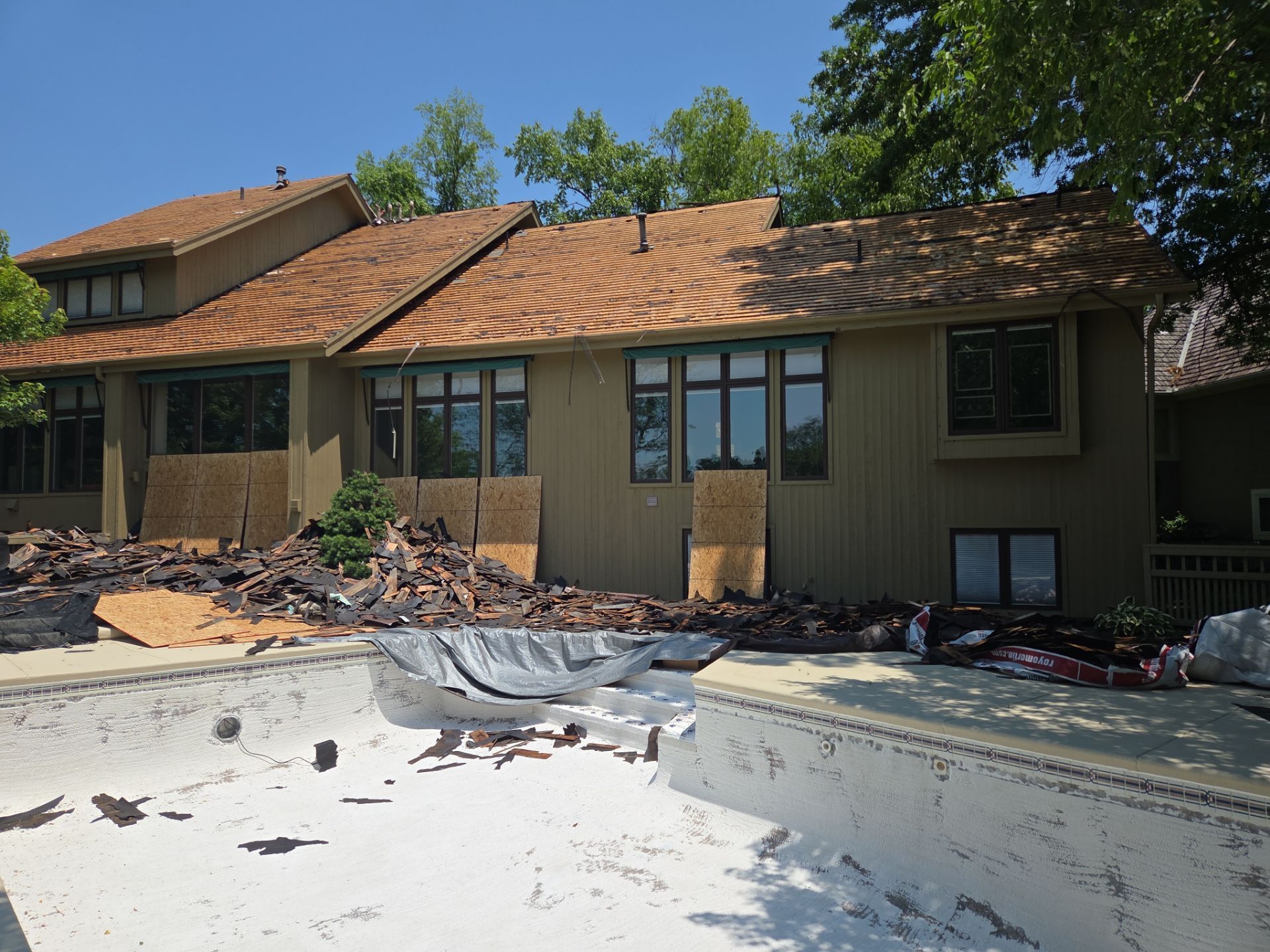 House with pool under renovation; debris surrounds empty pool; brown roof, green siding.