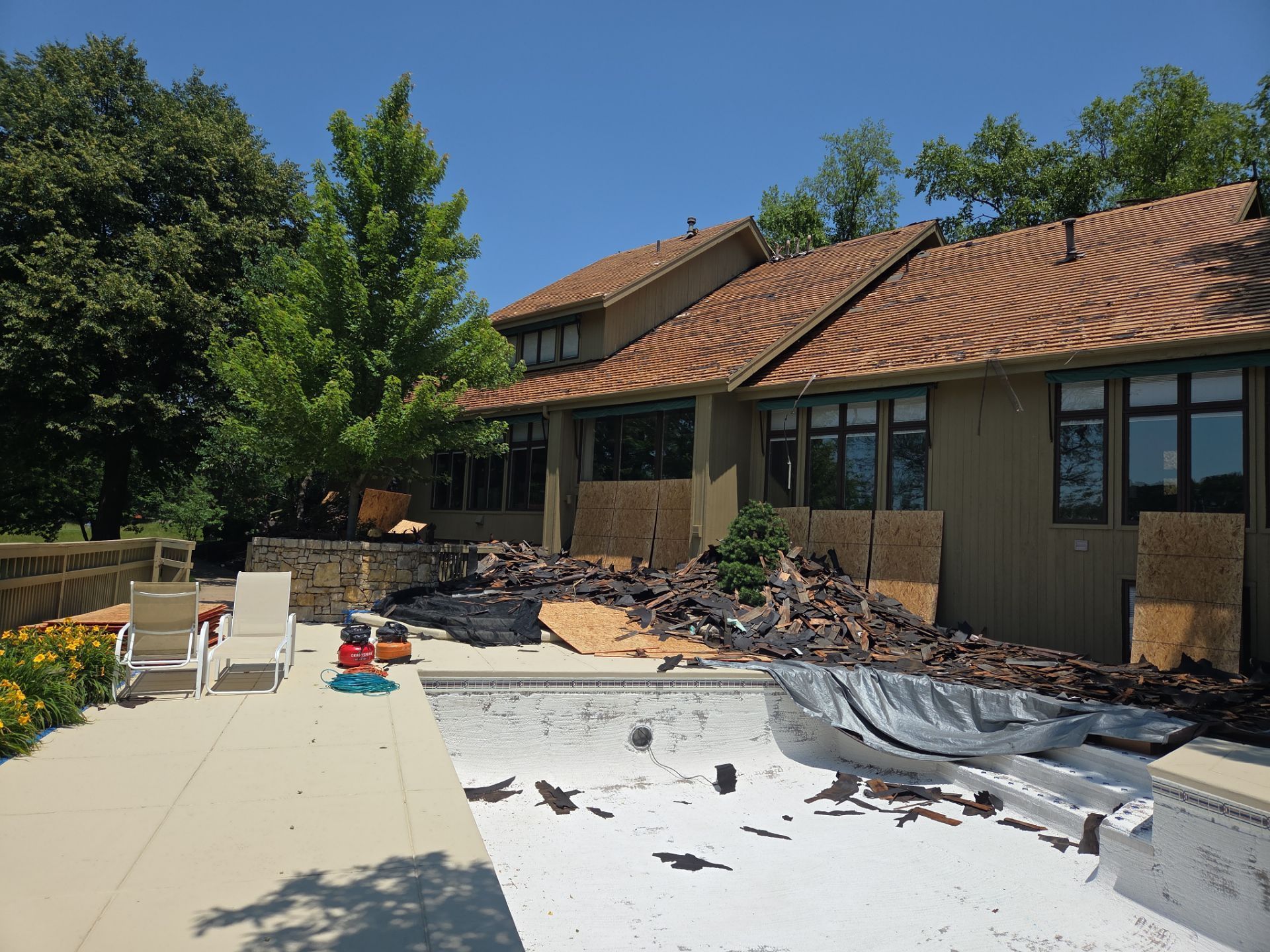 Backyard with home under construction, empty pool, wood debris, trees, and bright blue sky.