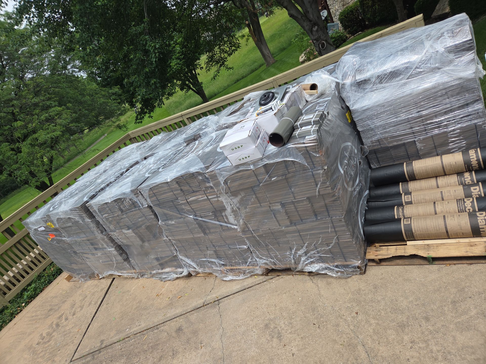 Pallets of asphalt shingles and rolled roofing materials on a driveway, ready for roof installation.