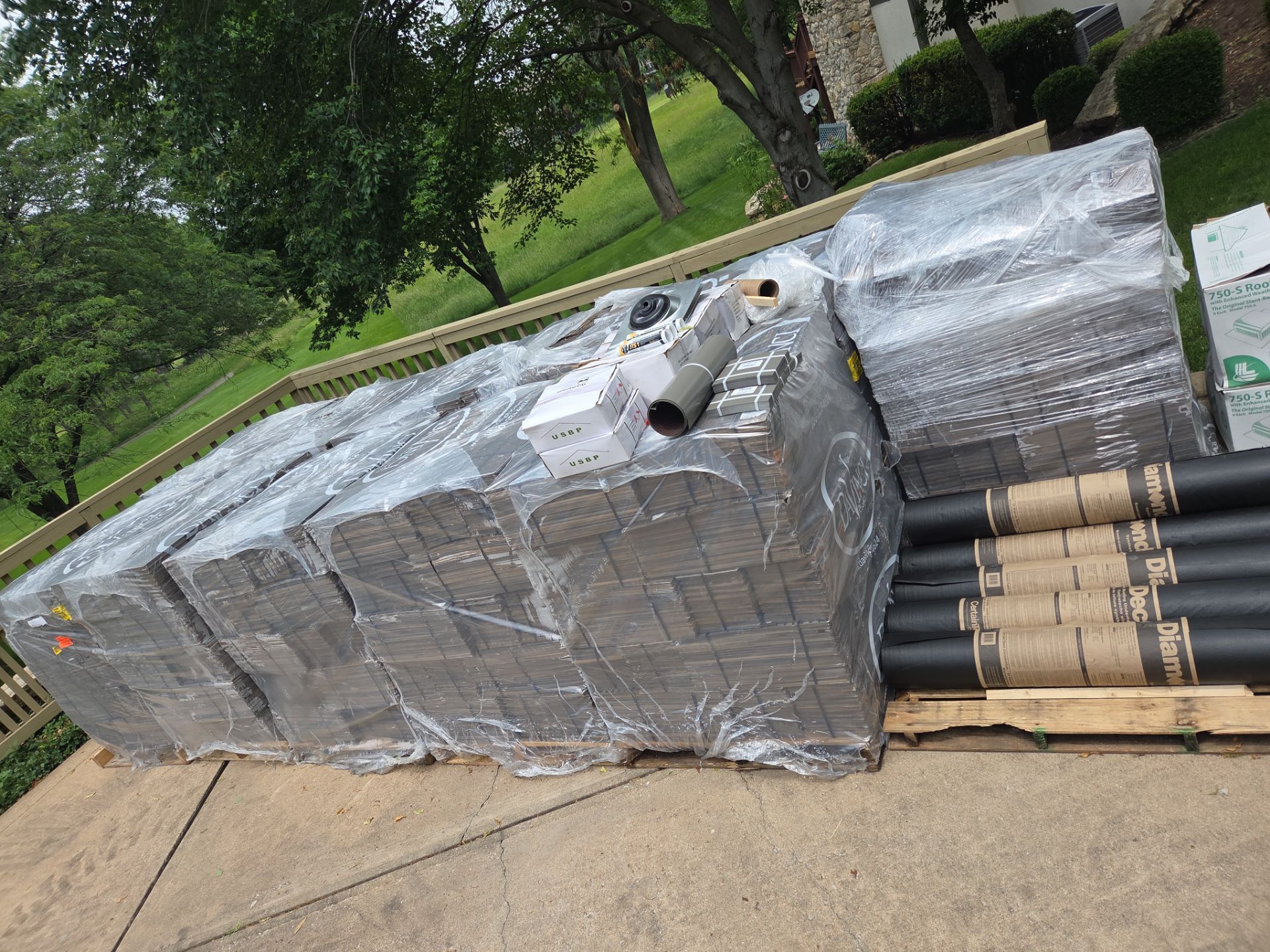 Pallets of roofing materials wrapped in plastic on a driveway, ready for installation.