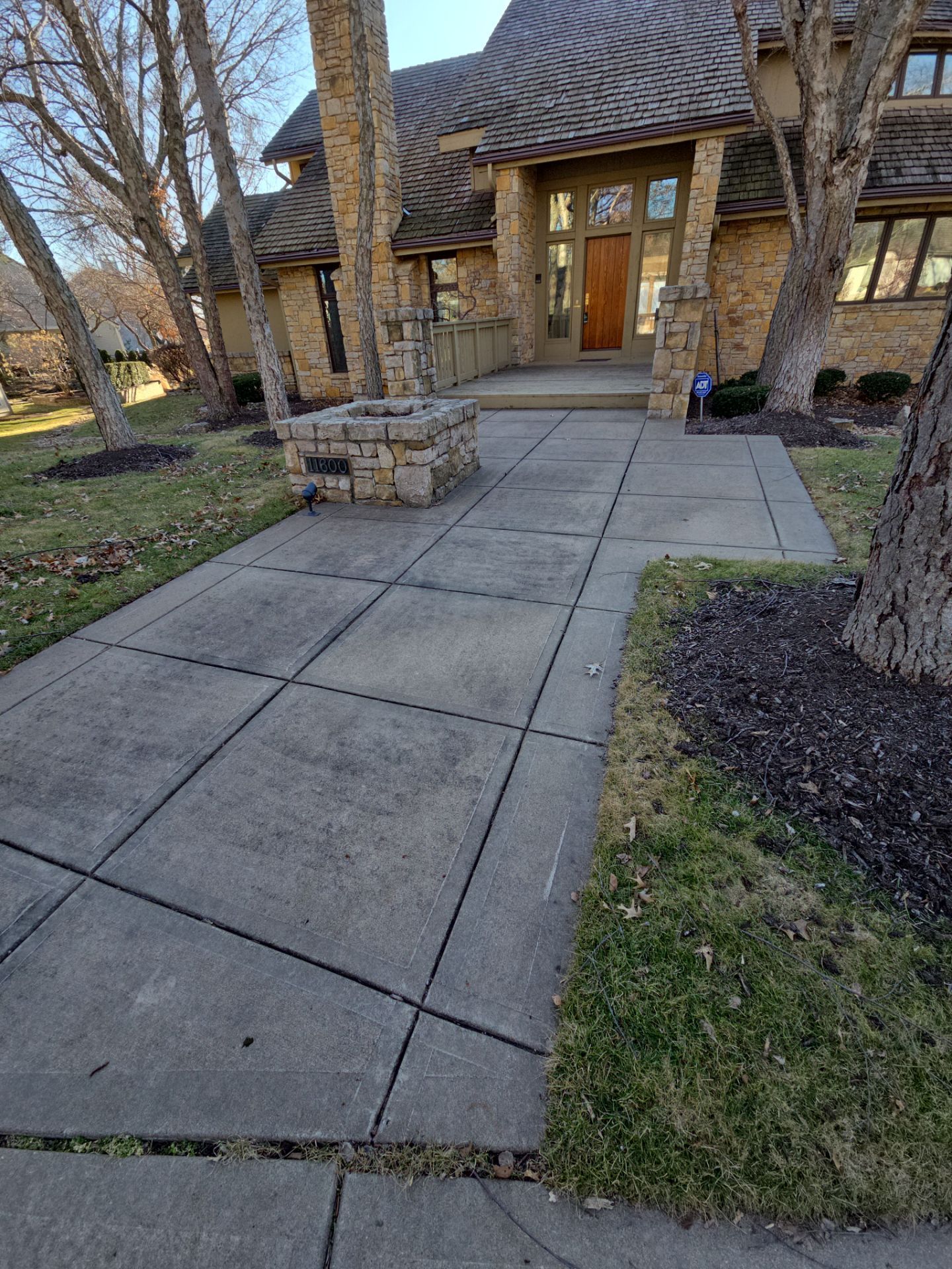 Stone walkway leading to a house with trees and a small stone structure.