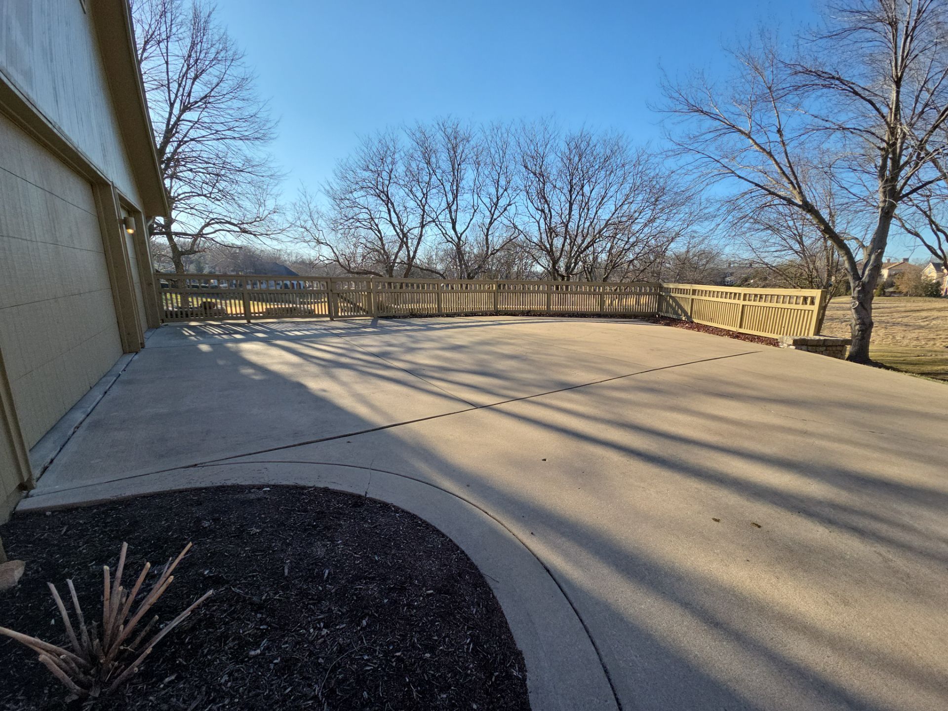 Concrete patio next to beige building with wooden fence and bare trees.