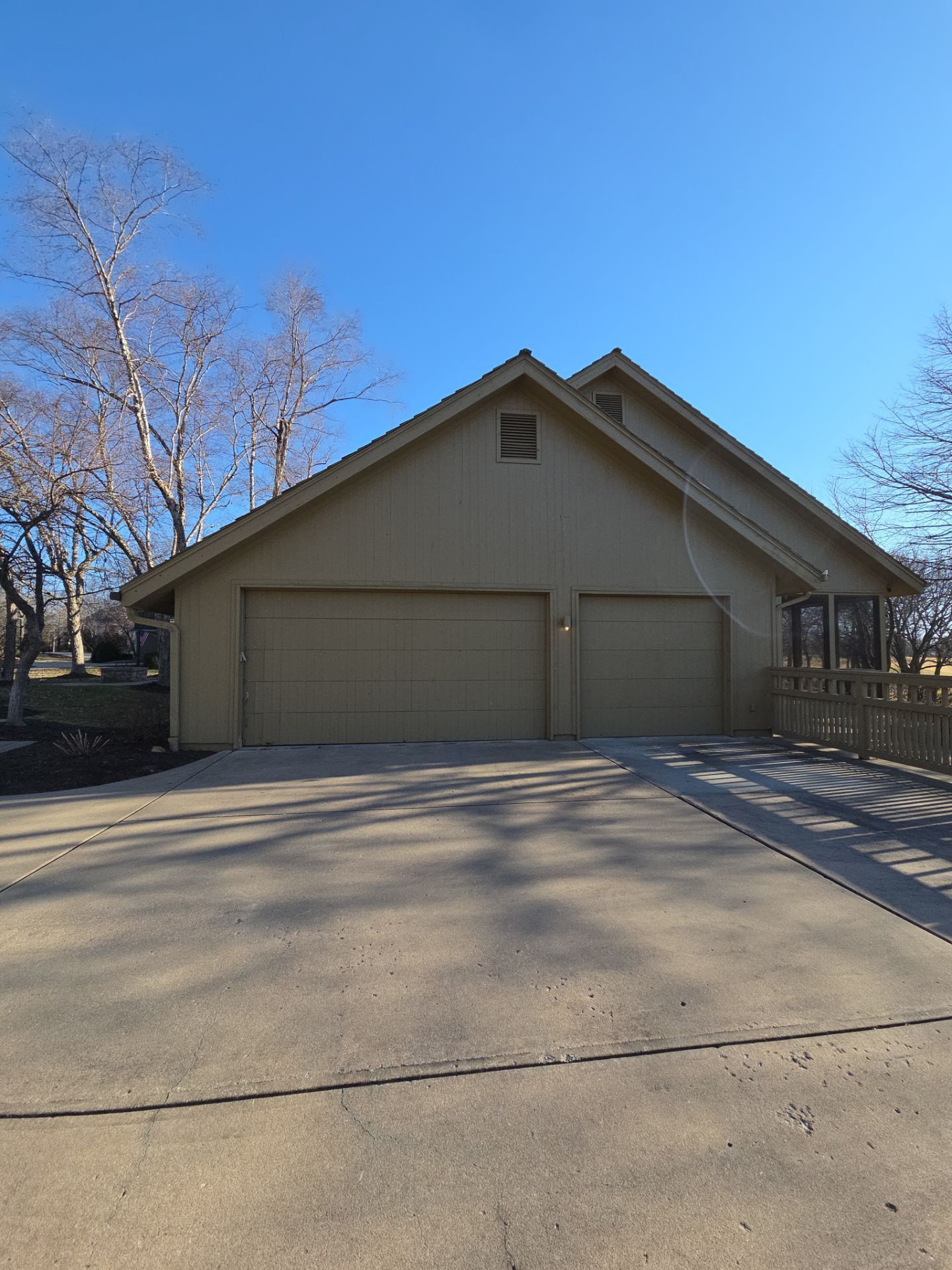 Tan two-car garage with driveway under a clear blue sky, surrounded by bare trees.