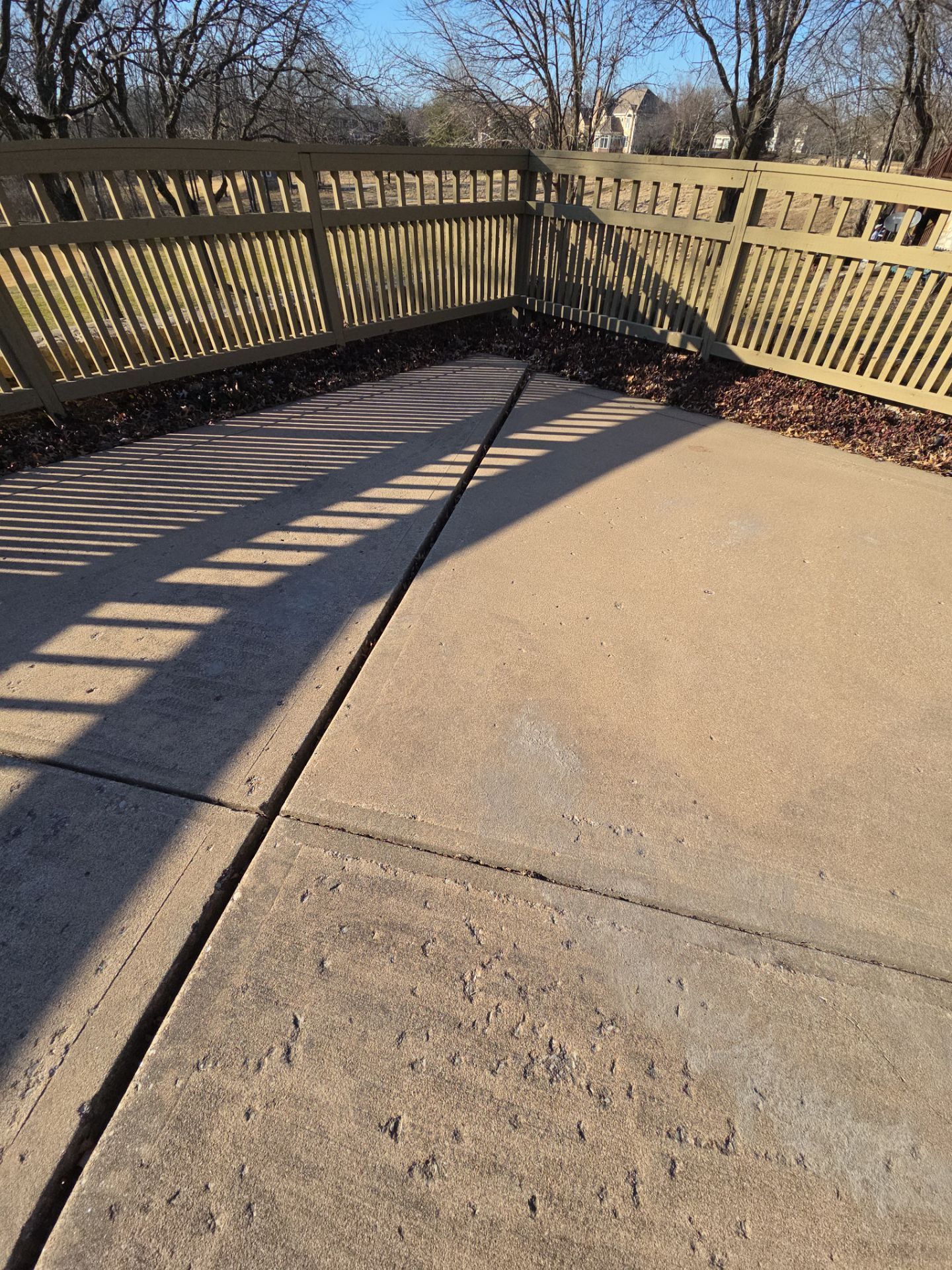 Concrete patio with a crack, wooden fence in the background.