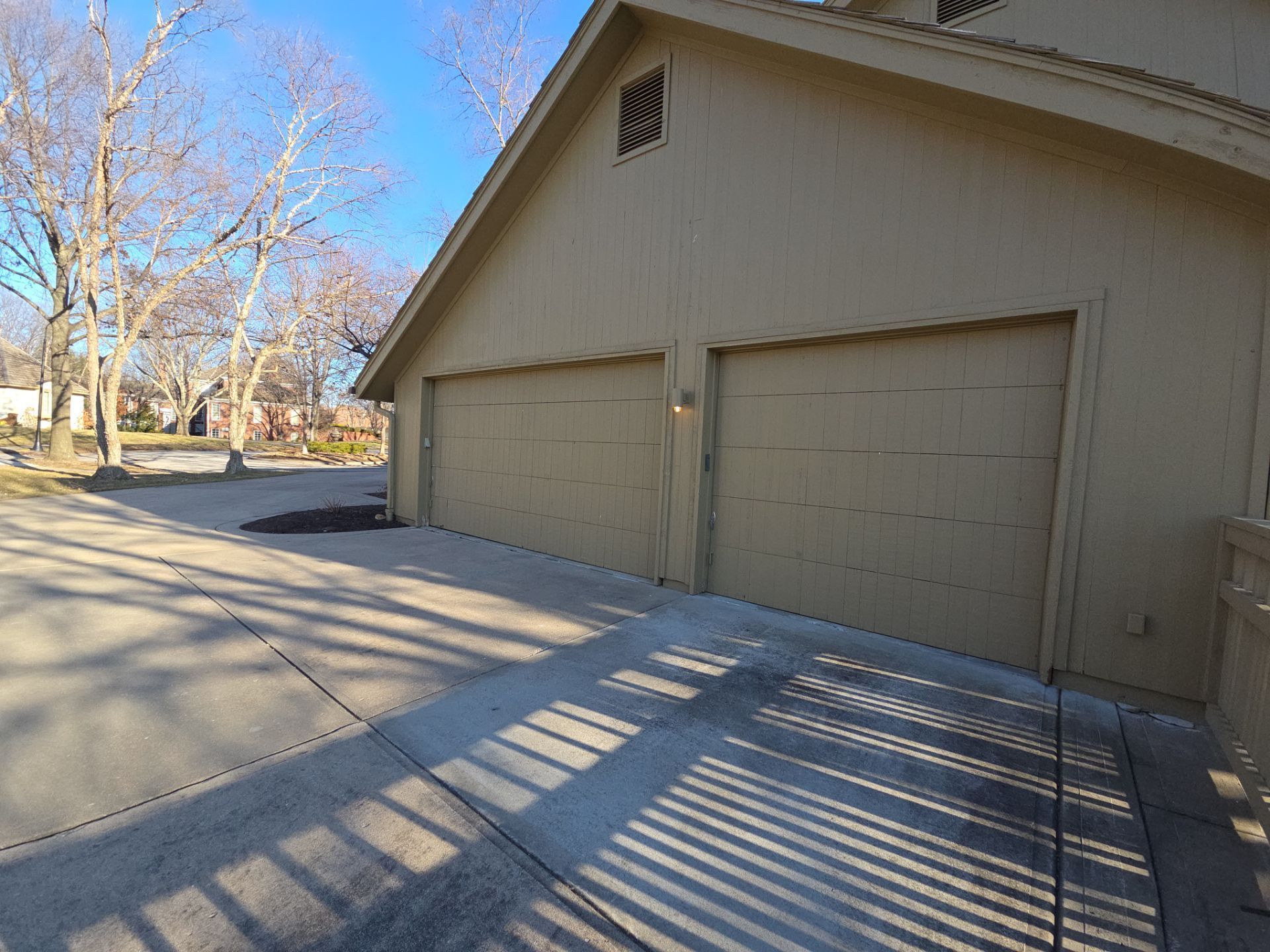 Garage with two doors, beige siding, and a concrete driveway on a sunny day.