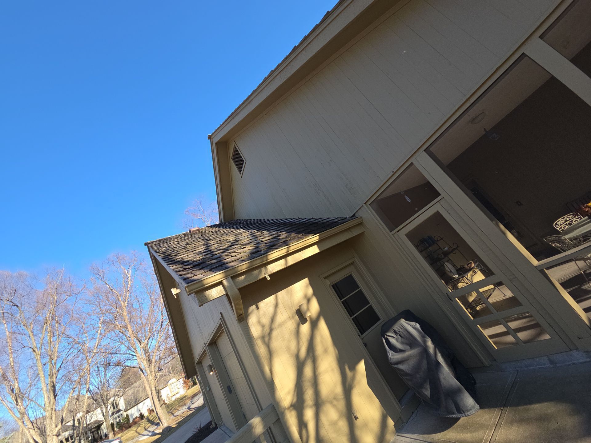 Beige house with a blue sky. Shadow cast on the side, covered patio to the right.
