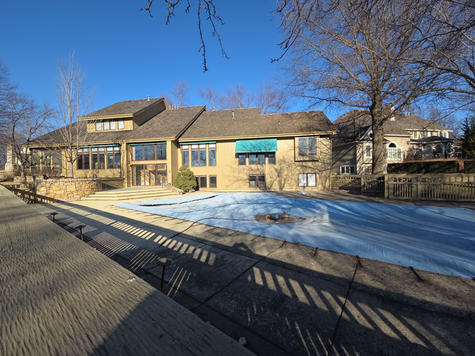 A multi-level beige house with a pool covered in blue, set under a clear blue sky.