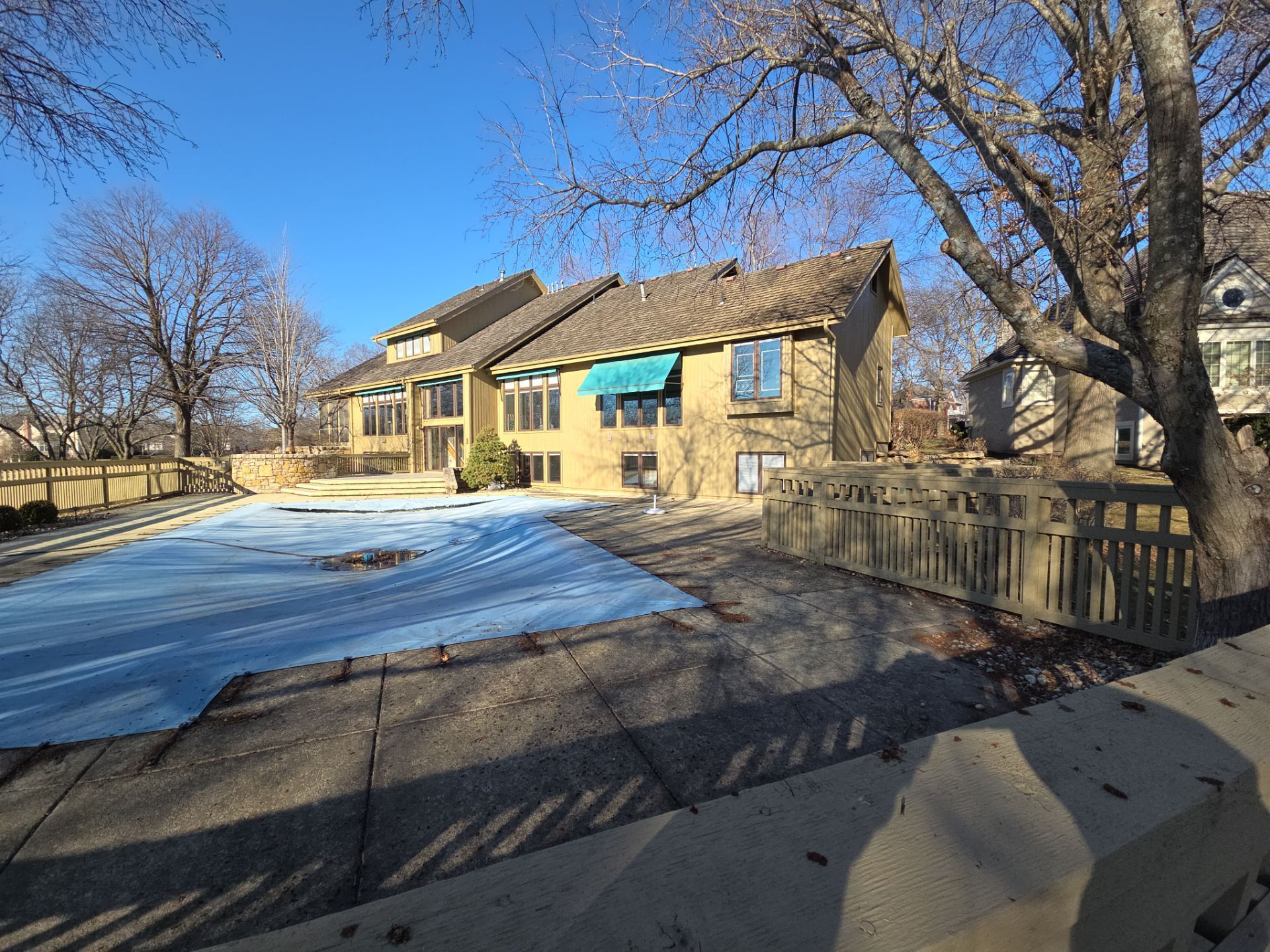 A house with a pool cover, trees, and a fence under a clear blue sky.