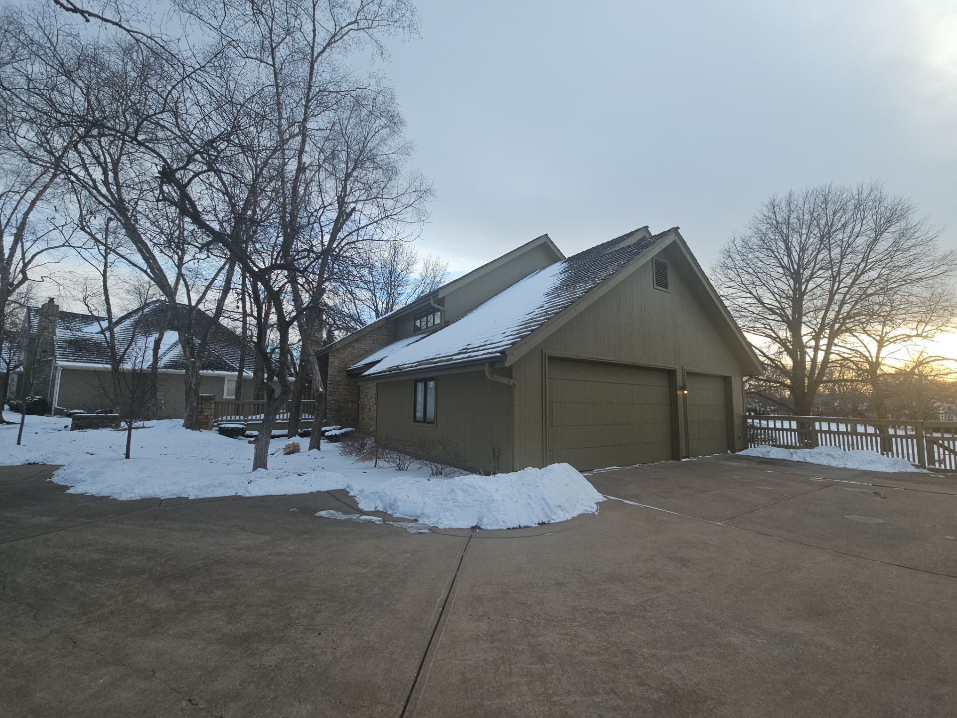 A two-car garage with snow on the roof and ground. Bare trees frame the building on a cloudy day.