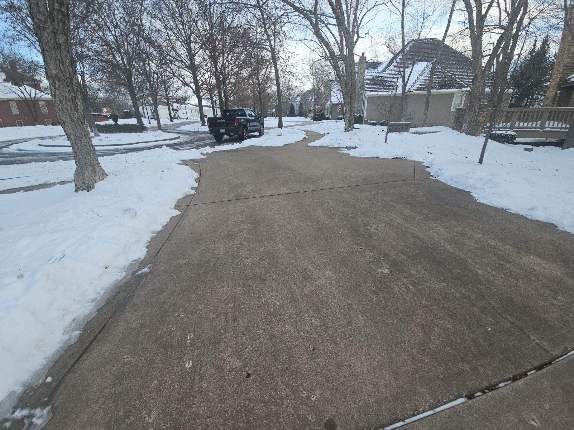 Snowy driveway with a black pickup truck. Trees line the street.