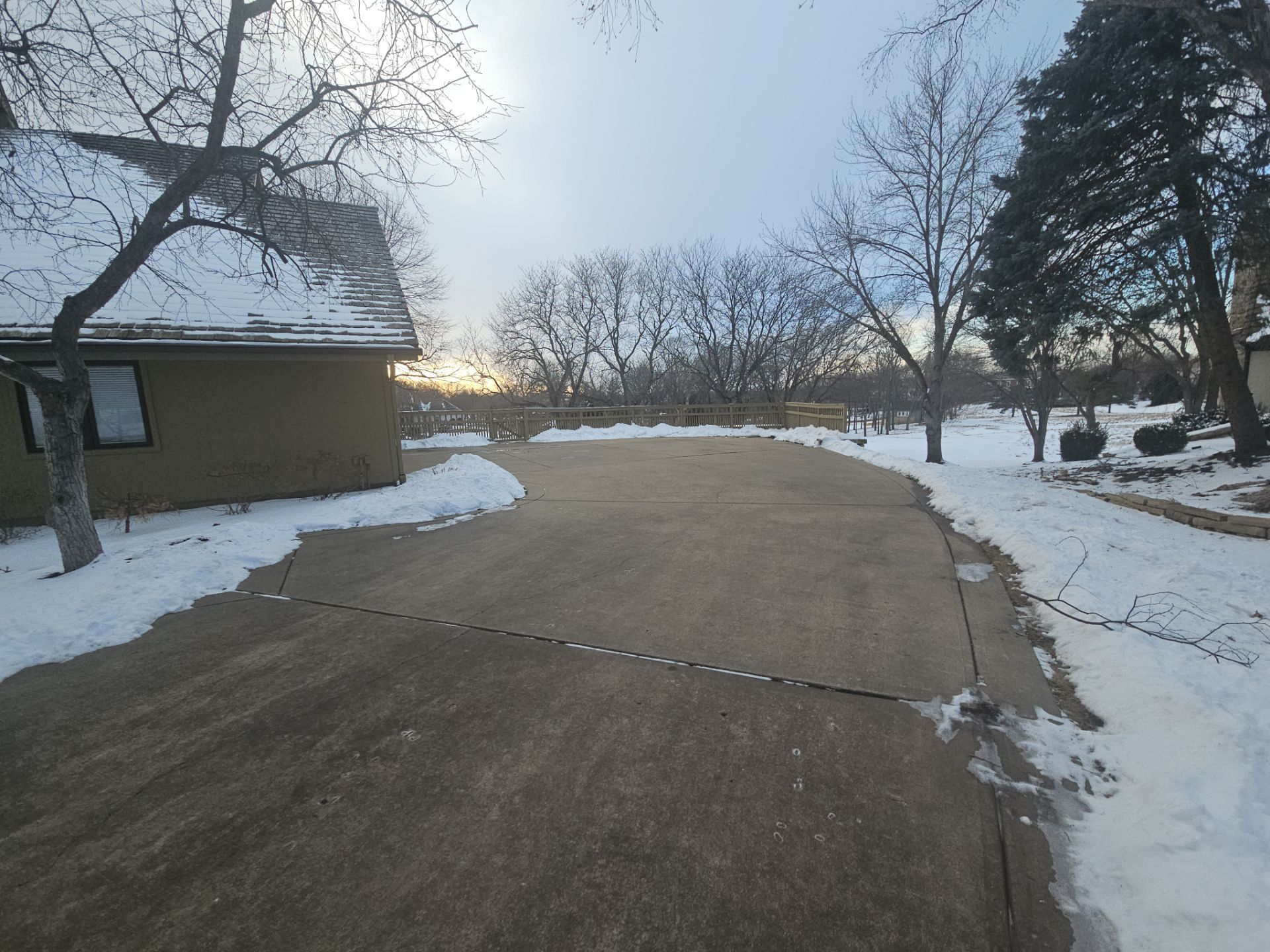 Winter scene: driveway partially covered in snow, trees, and a house.