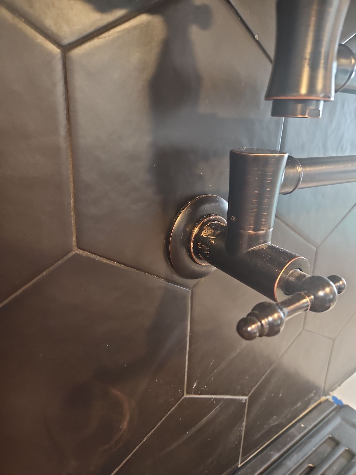 Close-up of dark brown faucet on a dark, hexagonal tile wall.