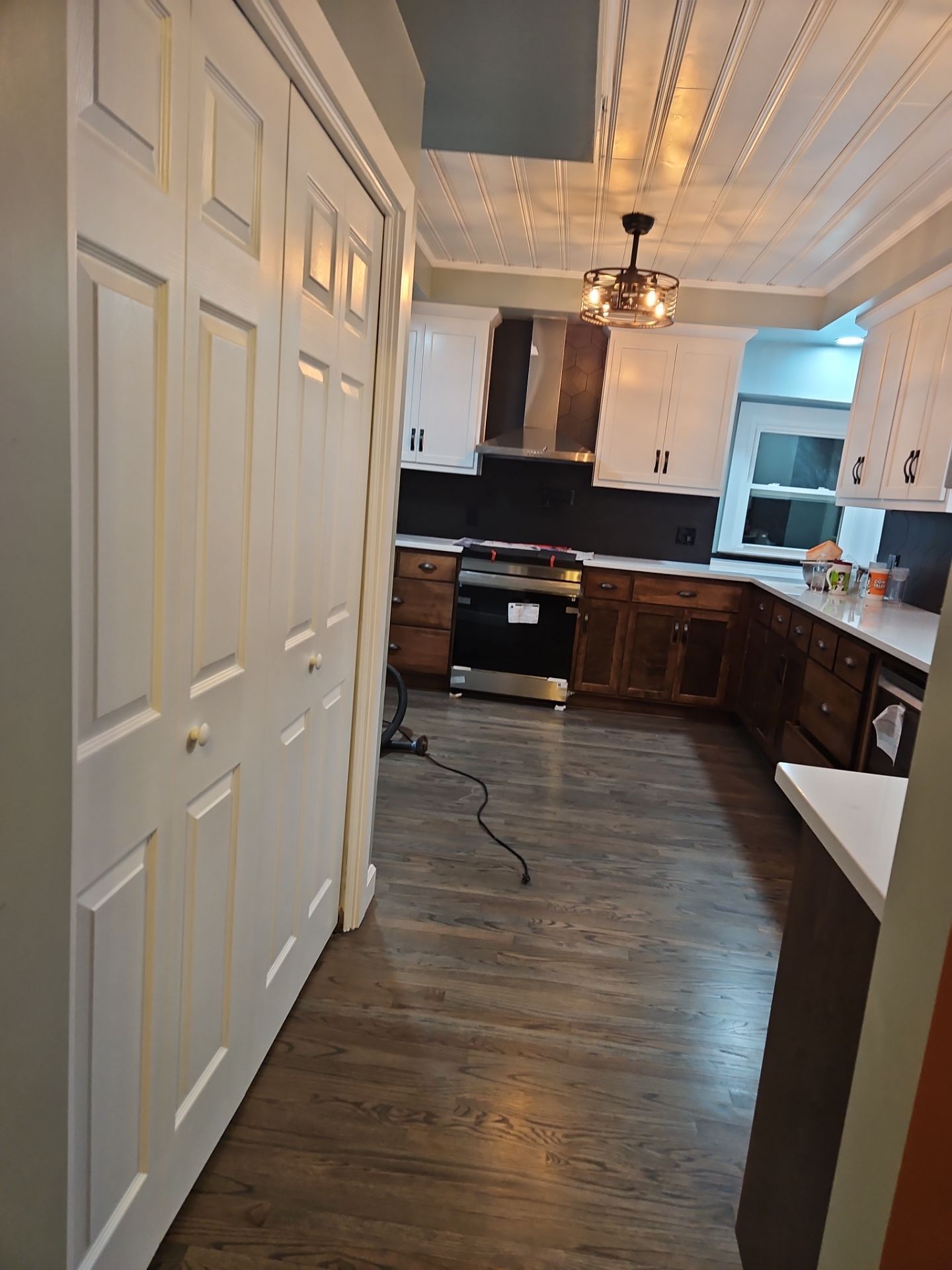 White bi-fold closet doors open to a kitchen with white and brown cabinets, hardwood floors, and a ceiling light.