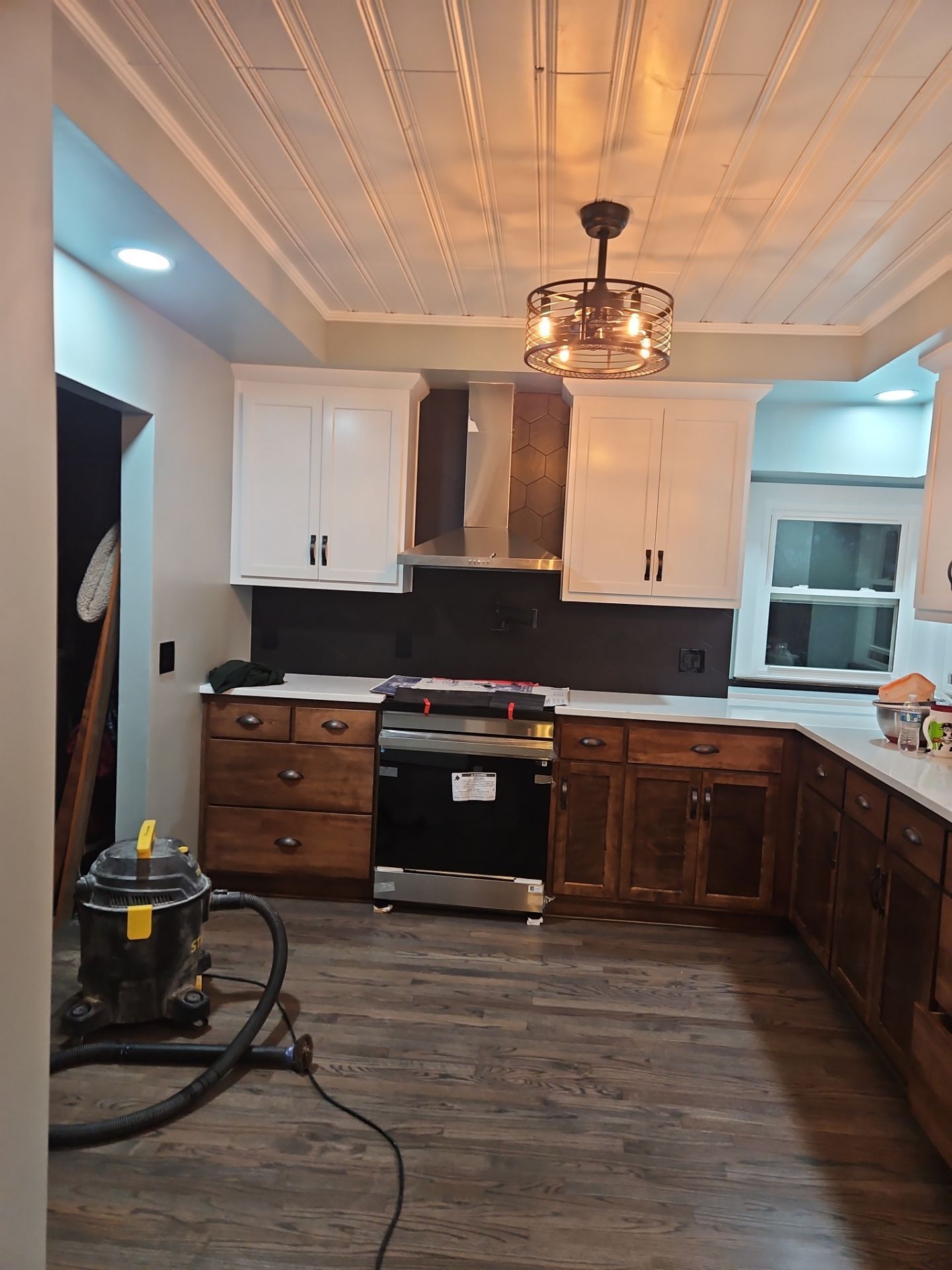 Kitchen with white upper cabinets, wooden lower cabinets, stainless steel range and hood, gray backsplash, and decorative ceiling.