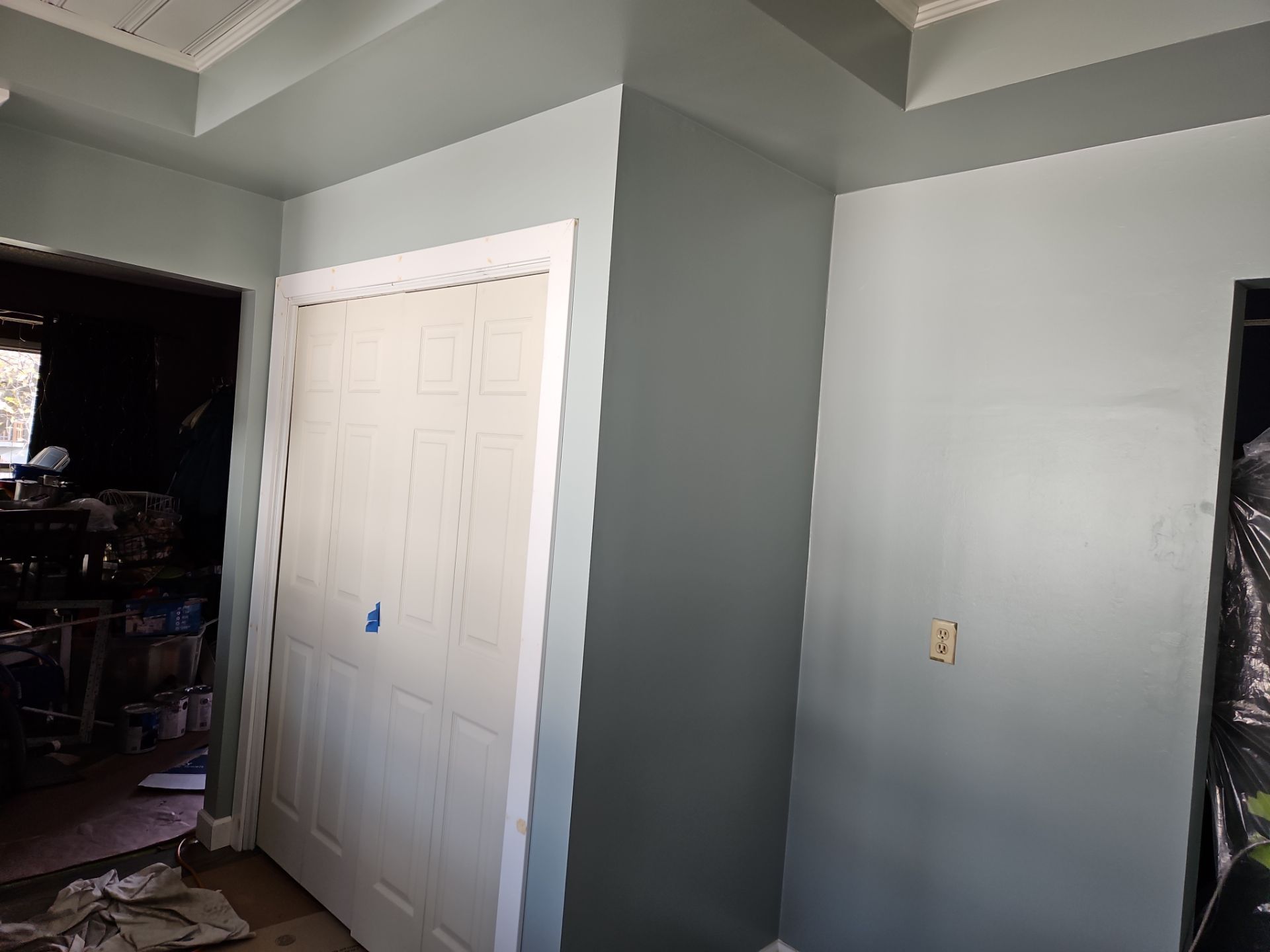 Gray-painted room with a white closet door and a dark doorway leading to a cluttered space.