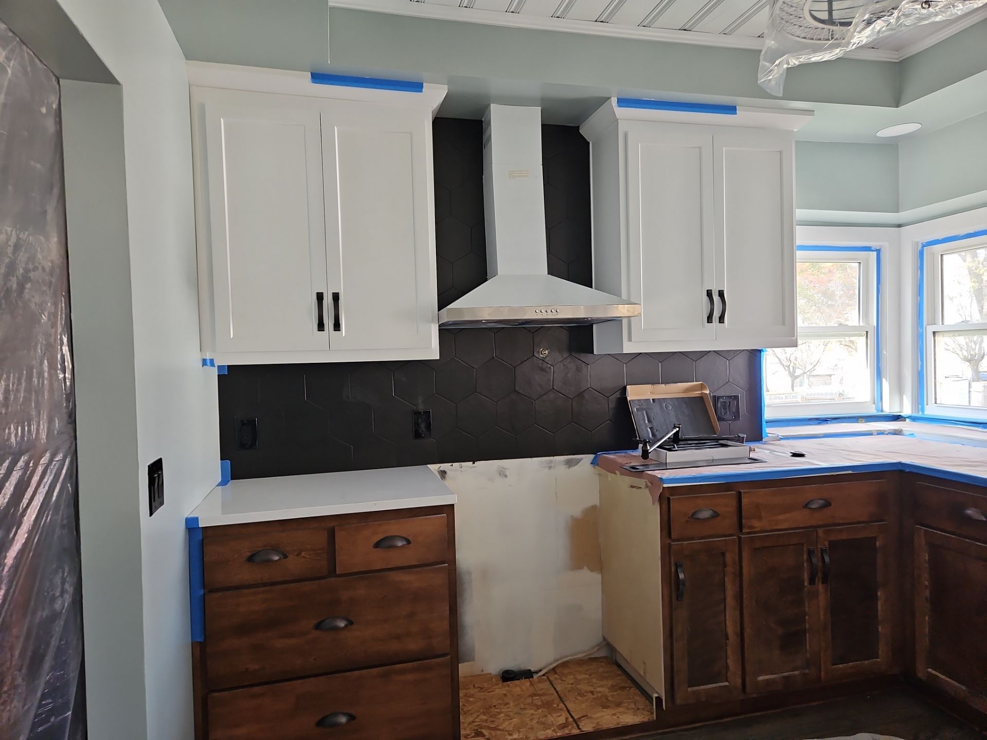 Kitchen renovation: white cabinets, black hexagon tile backsplash, brown lower cabinets, and a white range hood.