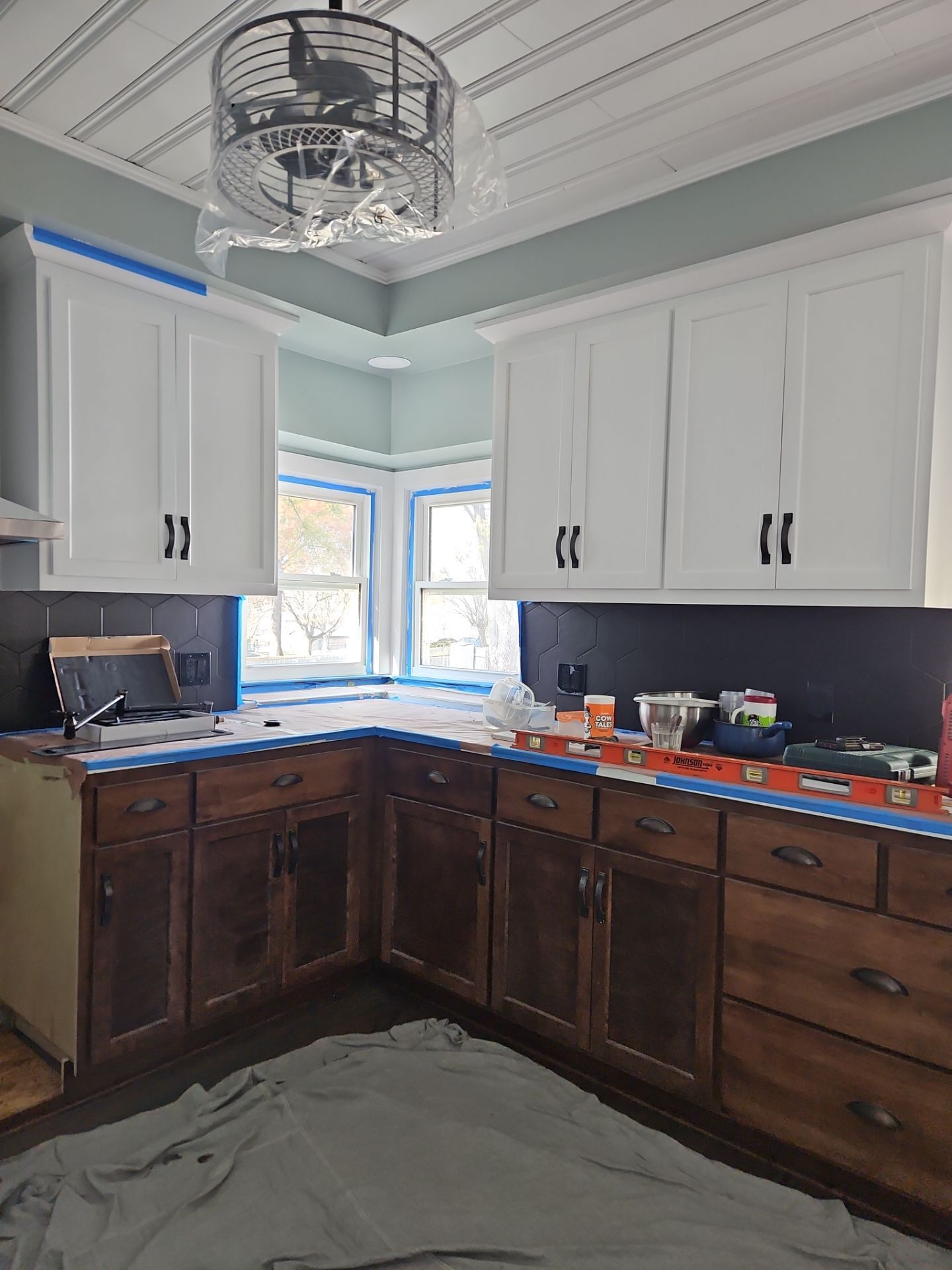 Kitchen remodel: white upper cabinets, dark brown lower cabinets, blue painter's tape, green wall, and gray floor covering.