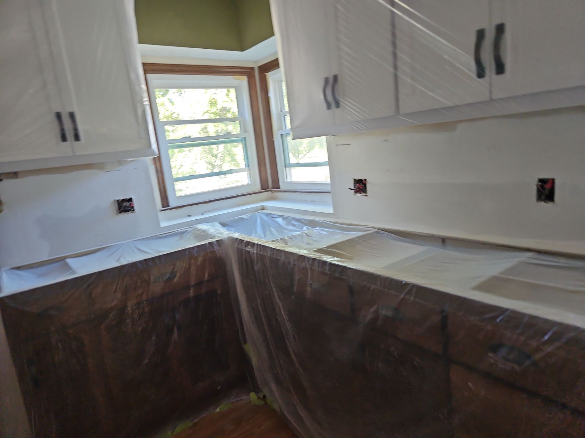 Kitchen with white cabinets and brown cabinetry; all protected with plastic during renovation.