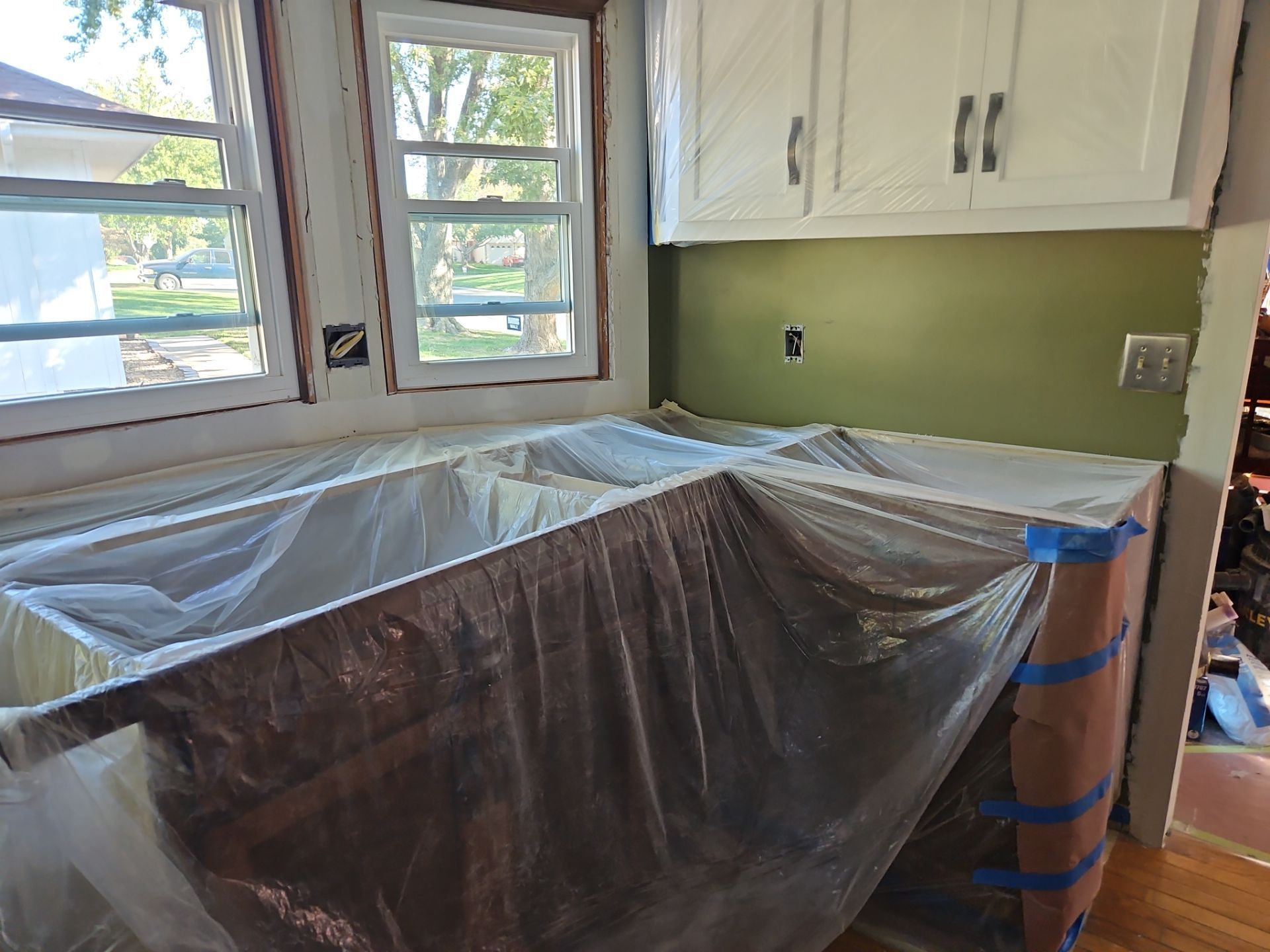 Kitchen counter covered with plastic sheeting during renovation, green backsplash, white cabinets.