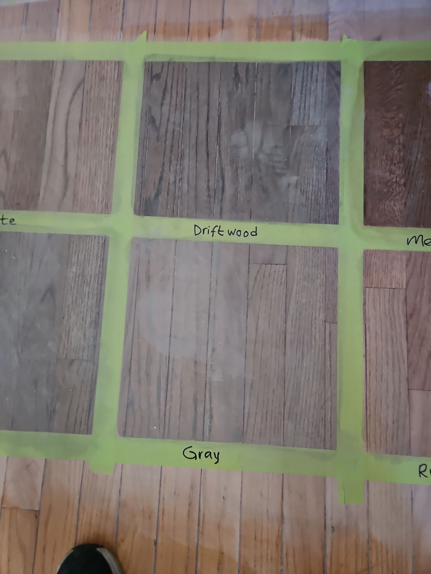 Samples of different wood-look flooring options, taped to a hardwood floor. The samples are labeled 