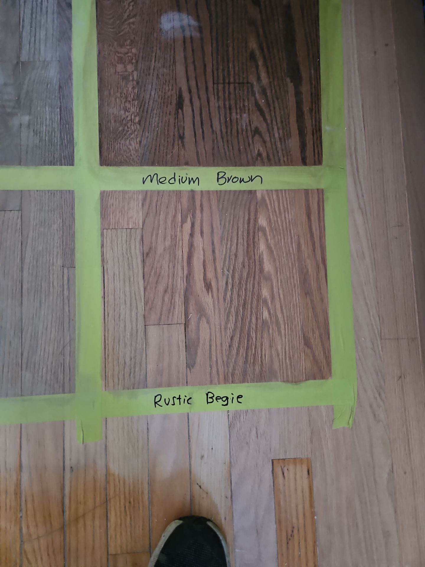 Hardwood floor samples taped onto a wooden floor, labeled 