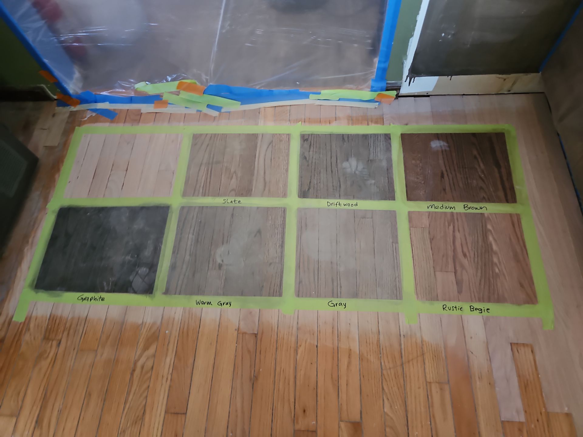 Floor with eight wood stain samples taped onto it; testing for color comparison.