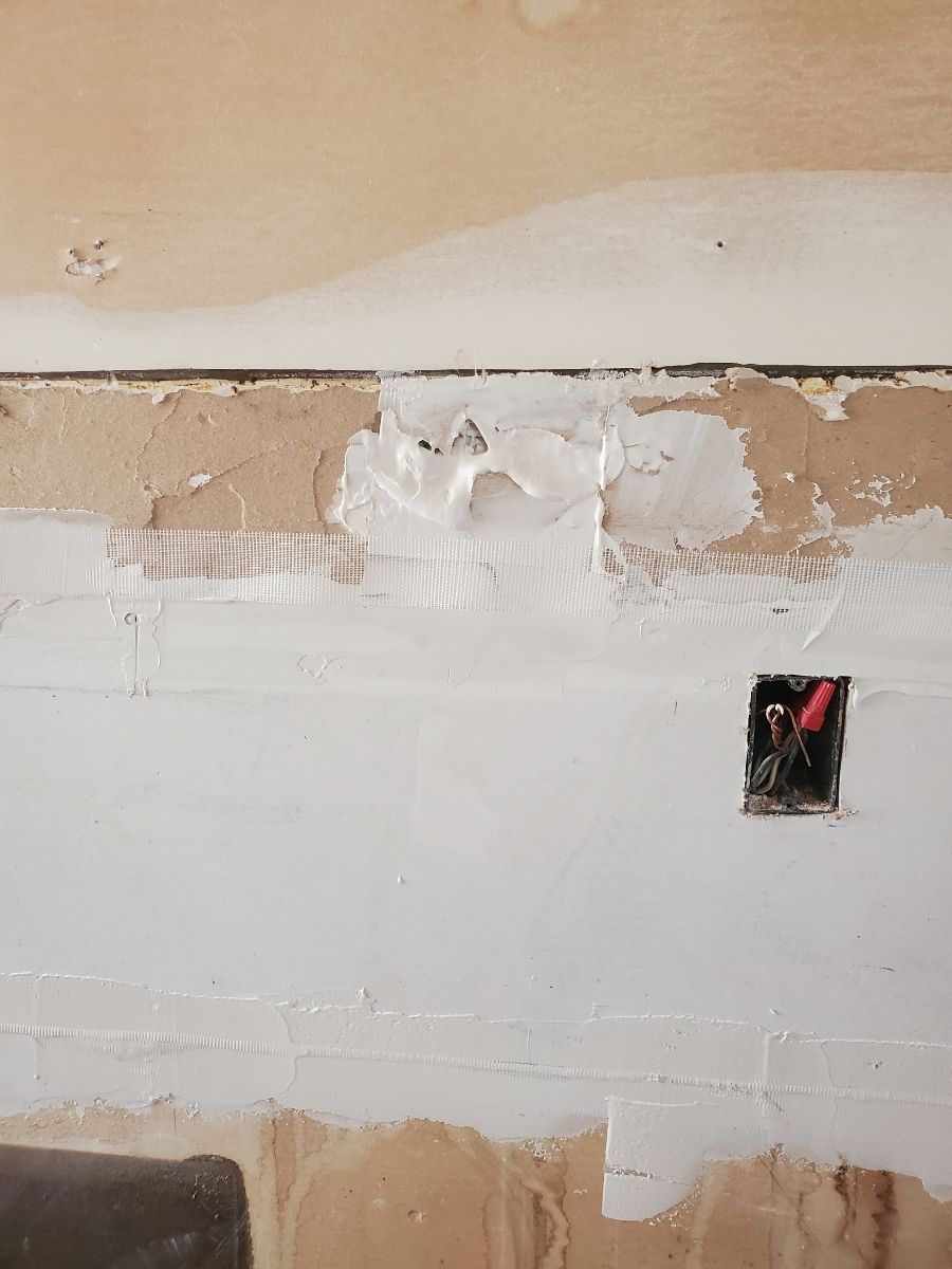 Wall with patched sections and an electrical outlet. White paint on brown wall.